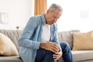 Mature man with arthritis knee pain sitting on couch at home