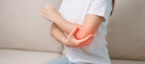 A woman is experiencing the pain of tennis elbow while relaxing on her living room couch.