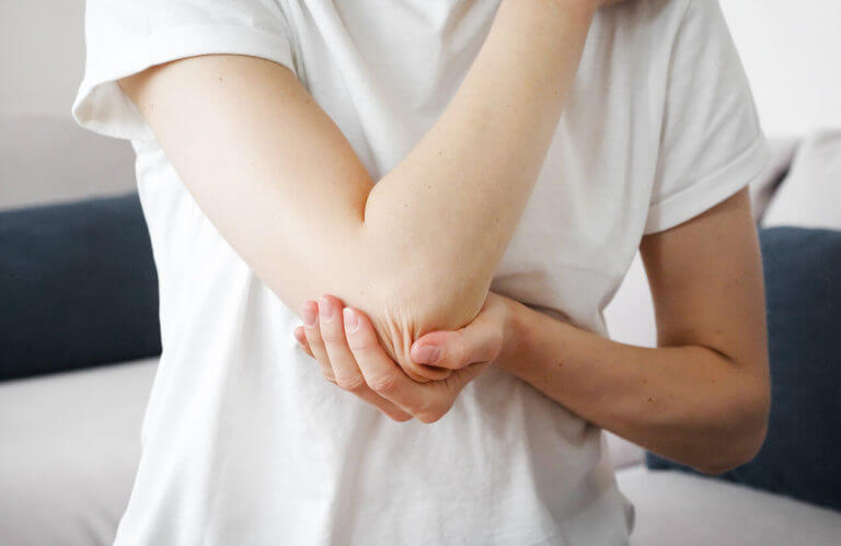 A woman suffering from elbow bone pain (Elbow Tendinitis) while in her bedroom.