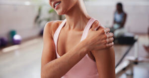 Image of a woman in the gym, clutching her shoulder due to pain from shoulder tendonitis during her workout.