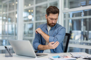 Businessman feeling acute elbow pain feeling like golfer's elbow, while working at office desk.